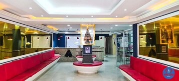 Un vestíbulo de hotel con mostrador de recepción, asientos rojos y una fuente decorativa.