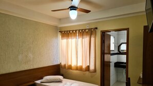 A hotel room with two single beds, a ceiling fan, a window with curtains, and a view of the bathroom and kitchen through an open door. - Hotel Sao Luiz (Aparecida)