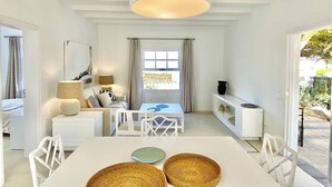 Quarto moderno e bem iluminado, com área de refeições, um conjunto de sofás e uma janela grande com cortinas.