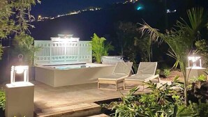 Uma área de piscina ao ar livre com espreguiçadeiras e degraus que dão acesso à piscina, cercada por vegetação.