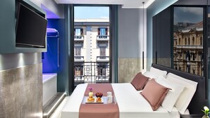 A modern hotel room with a large bed, a TV mounted on the wall, and a balcony with a city view. - Enjoy Art (Naples)
