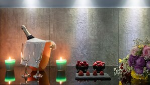 A table with a bottle of champagne, two glasses, two lit candles, and a floral arrangement. - Enjoy Art (Naples)