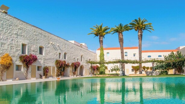 A pool with clear water, a stone building with arched windows, and palm trees. - Convento das Bernardas Lux T2 Triplex (Tavira)