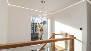 Un interior moderno con una escalera de madera, barandilla de cristal y una lámpara colgante.