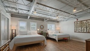 Ein geräumiges Zimmer mit zwei Betten, Holzboden, hoher Decke mit Metallbalken und einem an der Wand befestigten Kunstwerk.