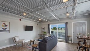 Ein geräumiges Wohnzimmer mit grauem Sofa, Holzboden, einem Flachbildfernseher und einem Essbereich mit Holztischen und einer Tischplatte.
