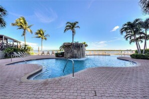 A swimming pool with a waterfall feature, surrounded by palm trees and lounge chairs. - Southern Comfort in Bonita Springs (Fort Myers Beach)