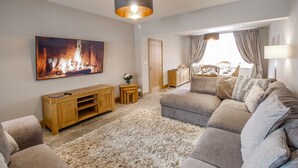 A living room with a grey sofa, a wooden entertainment unit, a fluffy rug, and a painting of a fire. - Family House (Weymouth)