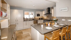 A modern kitchen with stainless steel appliances, a central island with seating, and a large window providing natural light. - Family House (Weymouth)