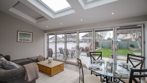 A modern living room with a glass dining table and chairs, a grey sofa, and a wooden coffee table. - Family House (Weymouth)