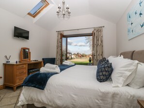 A bedroom with a bed, a desk, a TV, and a view of the outdoors.