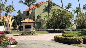 A large building with a red-tiled roof and arched windows, surrounded by palm trees and well-maintained landscaping. - Oceanview Villa - Steps Away from the Beach / Palmas del Mar Resort. (Palmas del Mar)