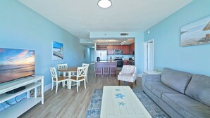 A living room with a TV, dining table, chairs, a sofa, and a kitchen in the background.