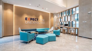 A modern lobby with a blue sofa, ottomans, and a wooden wall with a sign that reads "EXPECT THE UNEXPECTED." - Holiday Inn Express Linzhi Airport by IHG (Nyingtri)