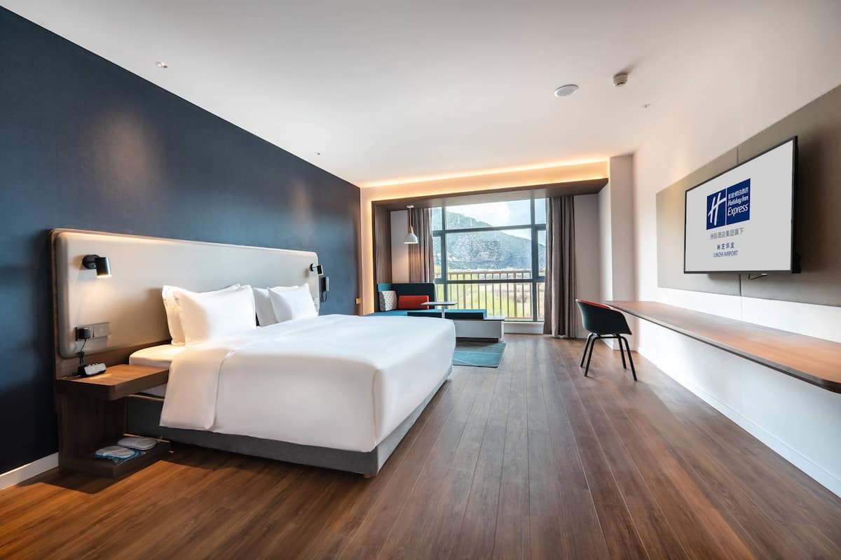 A modern hotel room with a large bed, a desk, and a TV mounted on the wall.