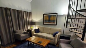 Ein modernes Wohnzimmer mit Couchtisch aus Holz, zwei Sofas, einem blauen Teppich und einer Wendeltreppe.