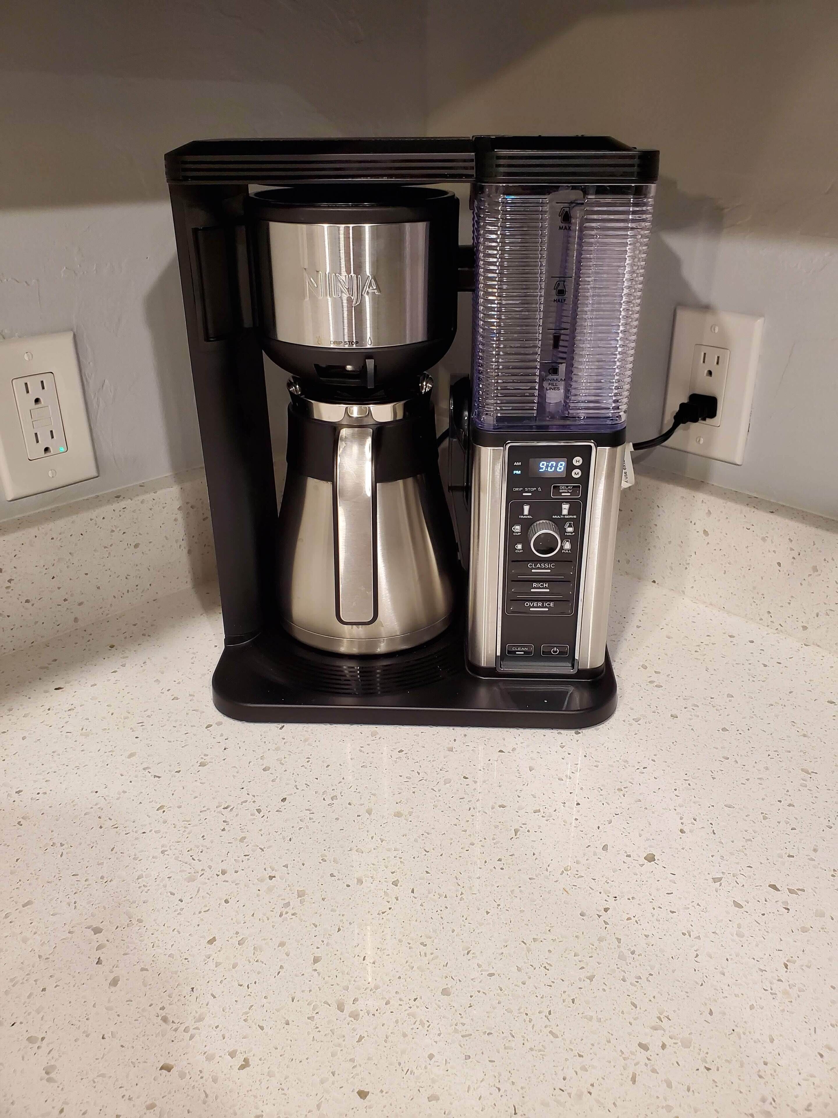 A coffee maker with a digital display and a water container on a kitchen counter.