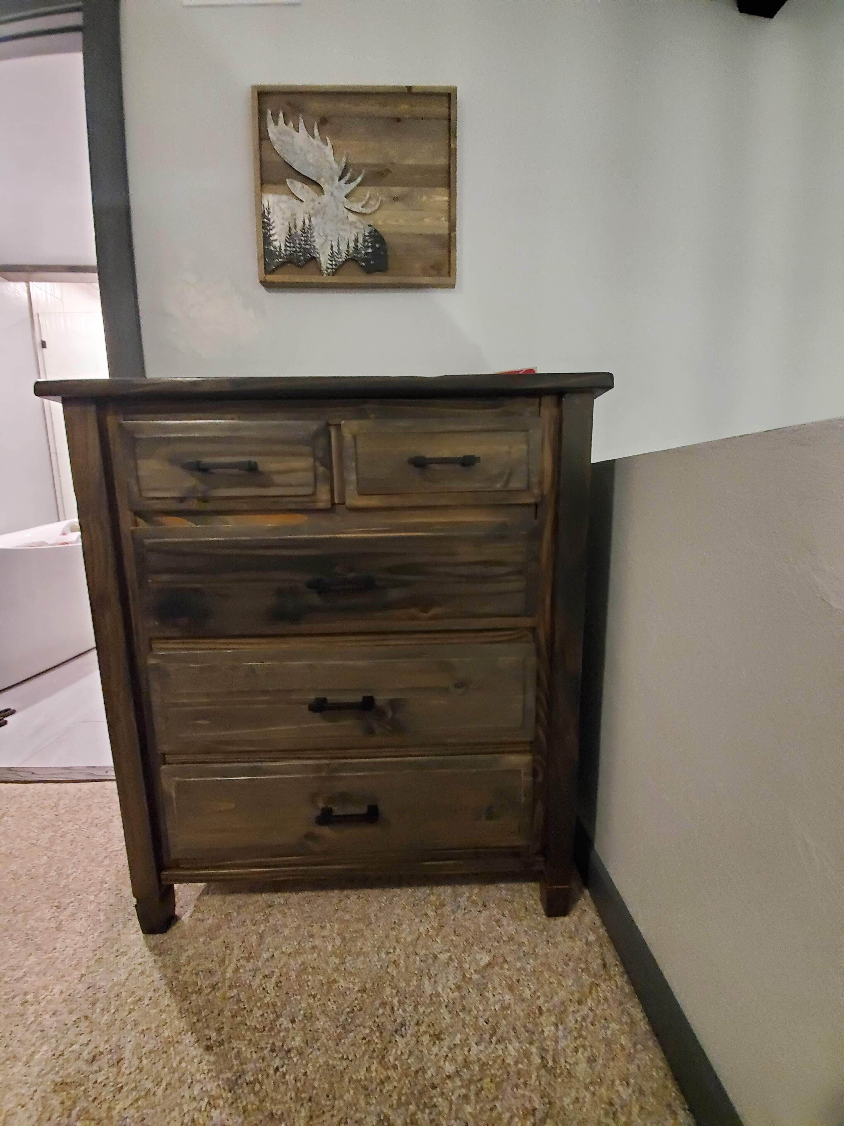 Eine Holzkommode mit Schubladen und einem kleinen dekorativen Gegenstand darüber an der Wand.
