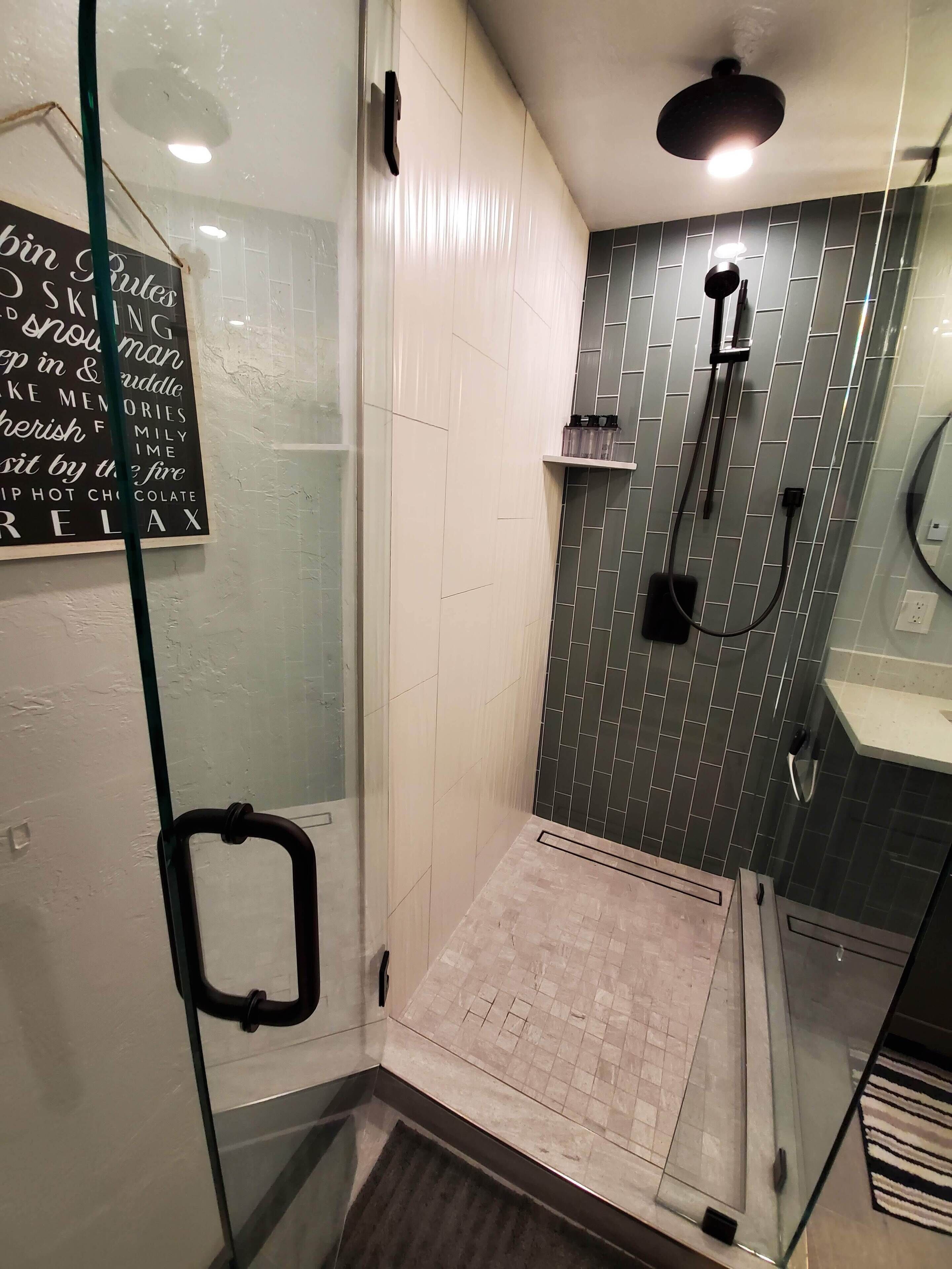 A modern bathroom with a glass shower enclosure, a black handheld showerhead, and a tiled shower wall.