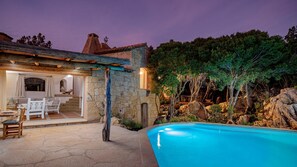 Uma casa de pedra com piscina, área de estar ao ar livre e escadaria para um andar superior.
