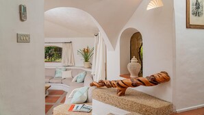 A modern interior with a curved wooden sculpture, a sofa with cushions, a potted plant, and a decorative vase. - Casa Chenal 10 Emma Villas (Arzachena)
