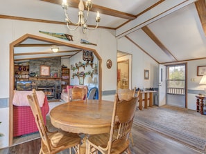 Cozy interior space with a round dining table, stone fireplace, and high ceiling with exposed beams.