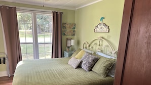 A bedroom with a large bed, a nightstand, a window with curtains, and a wall sign. - Country Farm House (Oberlin)