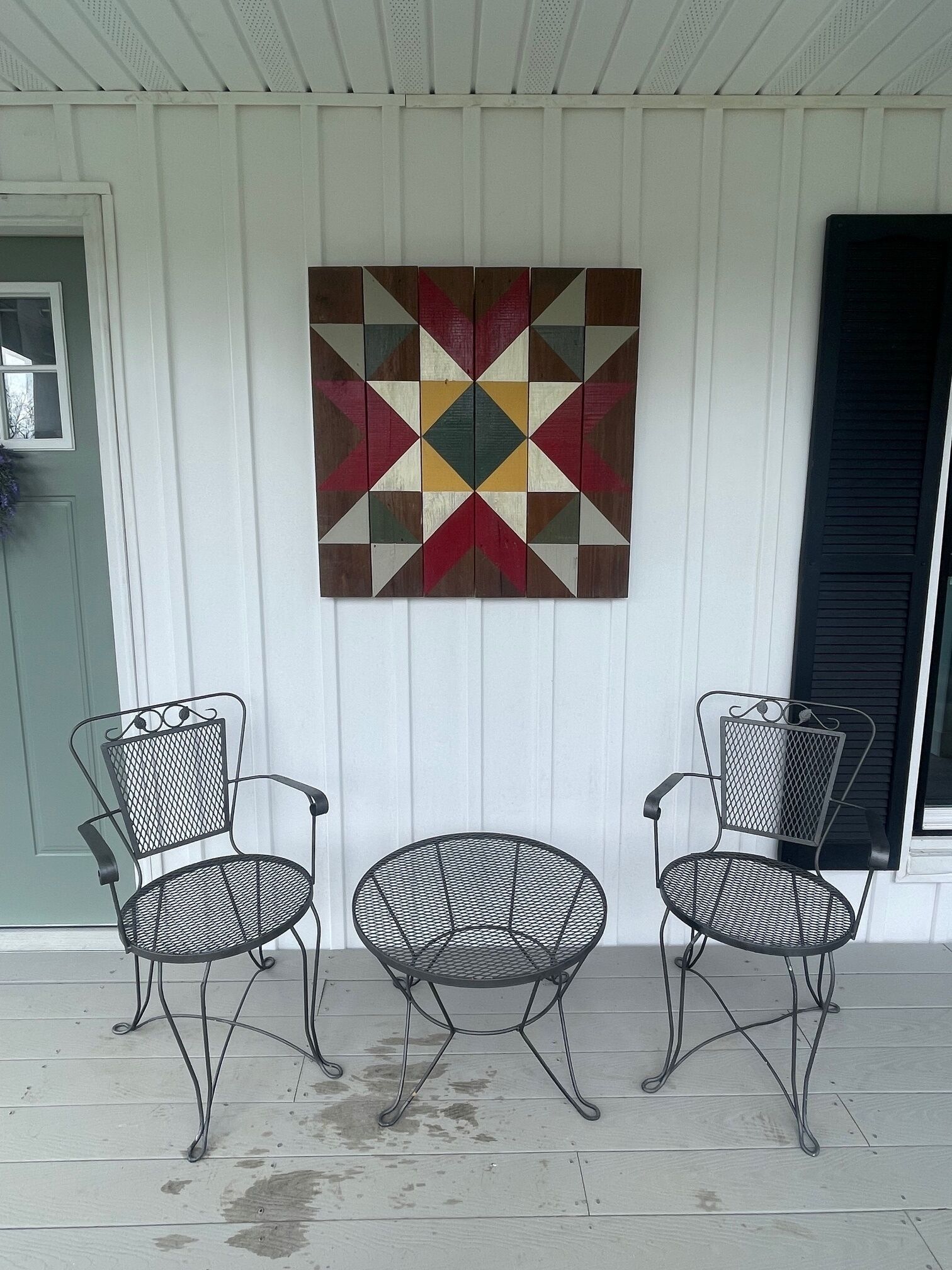 A porch with two metal chairs and a colorful quilt hanging on the wall.