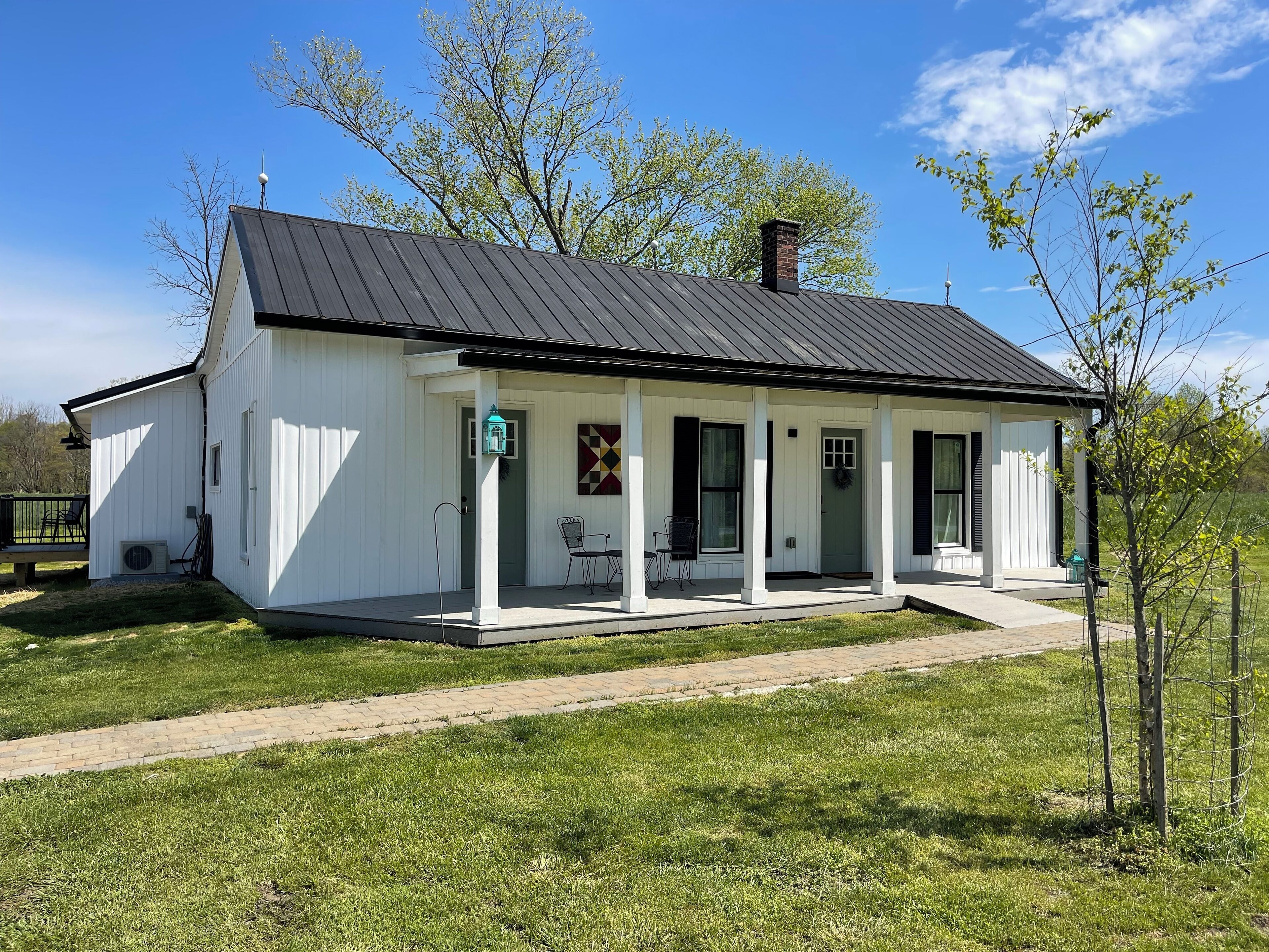 A white single-story house with a black roof, a front porch, and a small garden area.