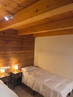 Una stanza con pareti e soffitto in legno, un letto con biancheria da letto bianca, un tavolino con una lampada e un lampadario a parete.