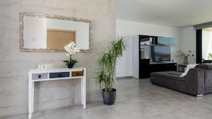 A modern living room with a white console table, a large mirror, a potted plant, a grey sofa, and a flat-screen TV. - YourHouse Casa Llubi,  house with private pool and air conditioning (Llubi)