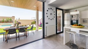A modern kitchen with a built-in clock, a dining area with a table and chairs, and a view of a swimming pool. - YourHouse Casa Llubi,  house with private pool and air conditioning (Llubi)