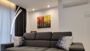 A modern living room with a grey sectional sofa, two patterned throw pillows, a floor lamp, and a colorful abstract painting on the wall. - Mediterranean Breeze Apartment (Xaghra)