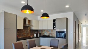 A modern kitchen with a central island, black pendant lights, and a stainless steel oven. - Mediterranean Breeze Apartment (Xaghra)