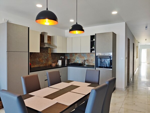 A modern kitchen with a central island, black pendant lights, and a stainless steel oven.
