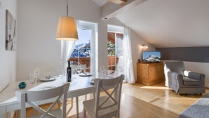 A dining area with a table set for four, a television on a wooden cabinet, and a view of a snowy mountain through a window. - Ski-in / Ski-out (Kirchberg in Tirol)