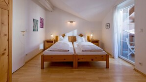 A bedroom with a wooden bed, two bedside tables with lamps, a large window, and a wooden door. - Ski-in / Ski-out (Kirchberg in Tirol)