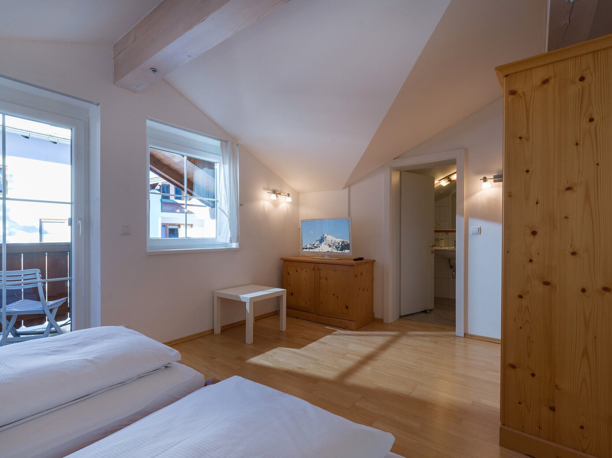 A bedroom with a bed, a small table, and a wooden wardrobe.