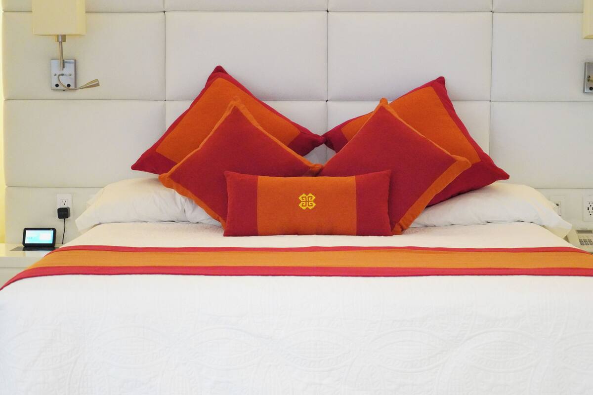 A bed with a white headboard, multiple pillows, and a red and orange striped blanket.