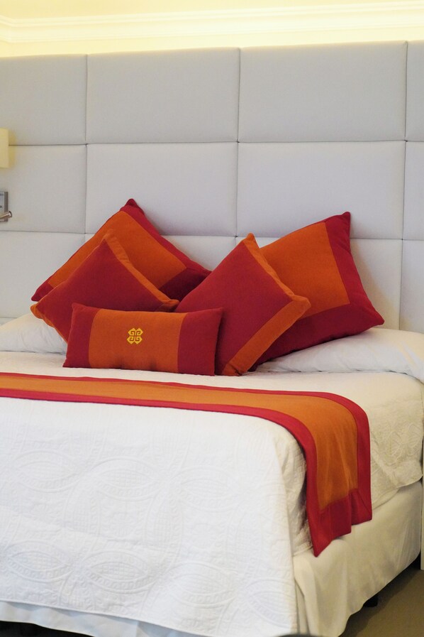 Una cama con cabecera blanca y varios almohadones rojos.