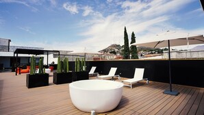 Terraza en la azotea con una bañera blanca grande, sillones de descanso y cactus.