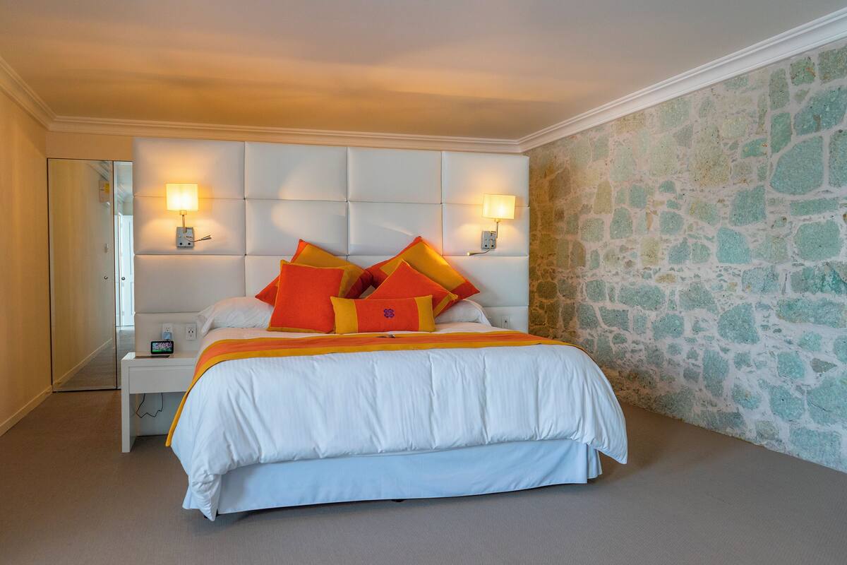 A hotel room with a large bed, white headboard, two bedside lamps, a nightstand, and a stone accent wall.
