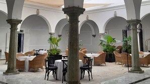 Un patio amplio con arcos blancos, columnas y mesas con sillas de mimbre.