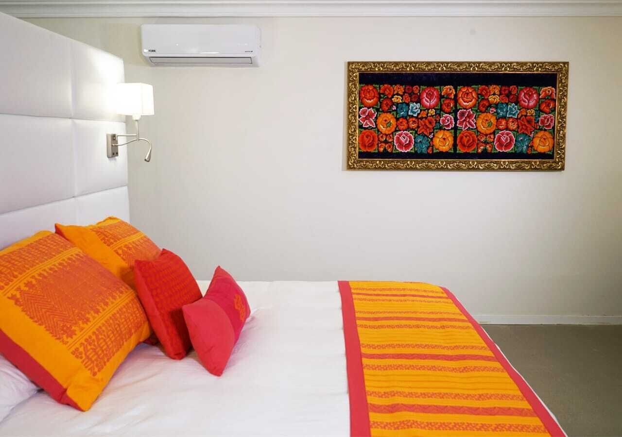 Habitación de hotel con cama, almohadas, aire acondicionado instalado en la pared y una obra de arte floral enmarco.