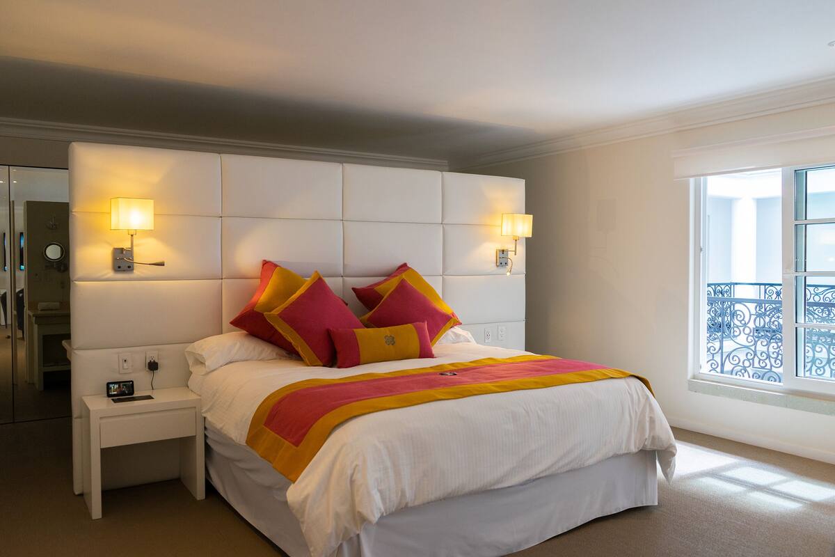A hotel room with a large bed, two bedside tables, and a window with a balcony view.