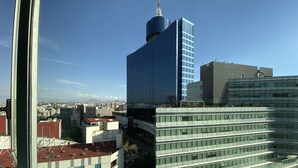 Un edificio moderno de gran altura con una fachada azul y blanca distintiva, rodeado de otros edificios y un cielo despejado.