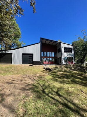 Un bâtiment moderne doté d’un grand portail de garage, d’un porche abrité avec des chaises rouges et d’une cour verdoyante.