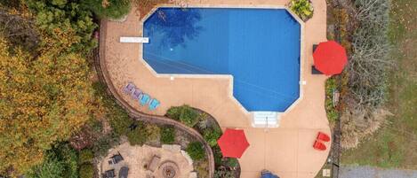 Vista aérea de una zona de piscina con solárium de arena, sillas de descanso y sombrillas.