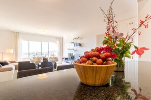 Una cocina moderna con un bol de frutas de madera en la encimera, un jarrón de flores y una zona de comedor con vistas.