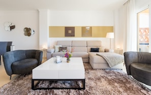 Ein modernes Wohnzimmer mit einem weißen Sofa, zwei Sesseln, einem Couchtisch und einem flauschigen Teppich.
